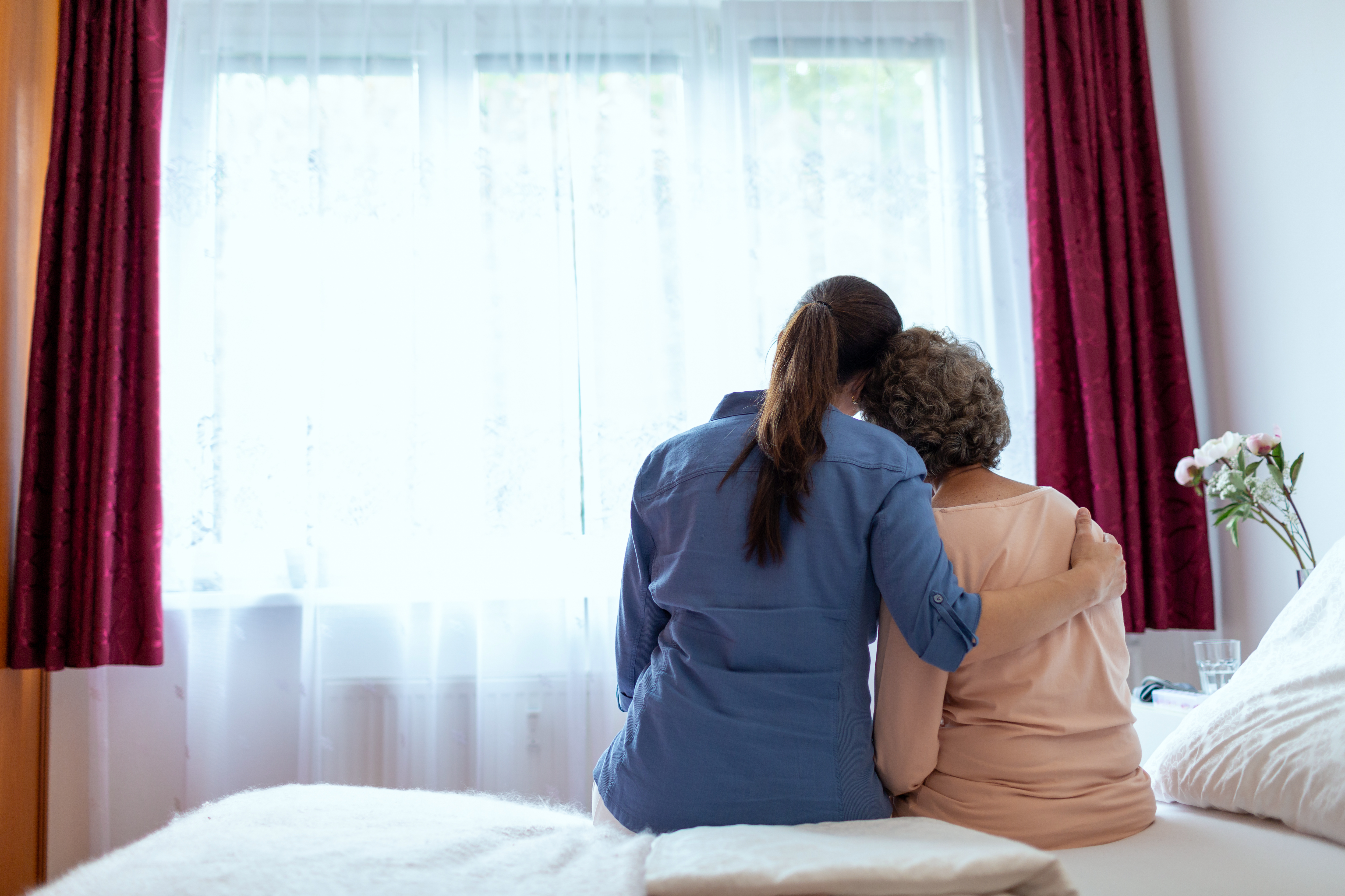 Female Home Nurse Hugging Elderly Woman on Bed.